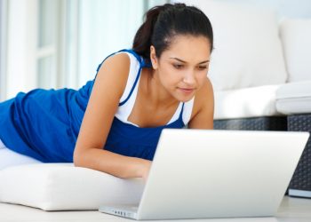 Portrait of beautiful young girl lying on floor and using a laptop at home - Indoor